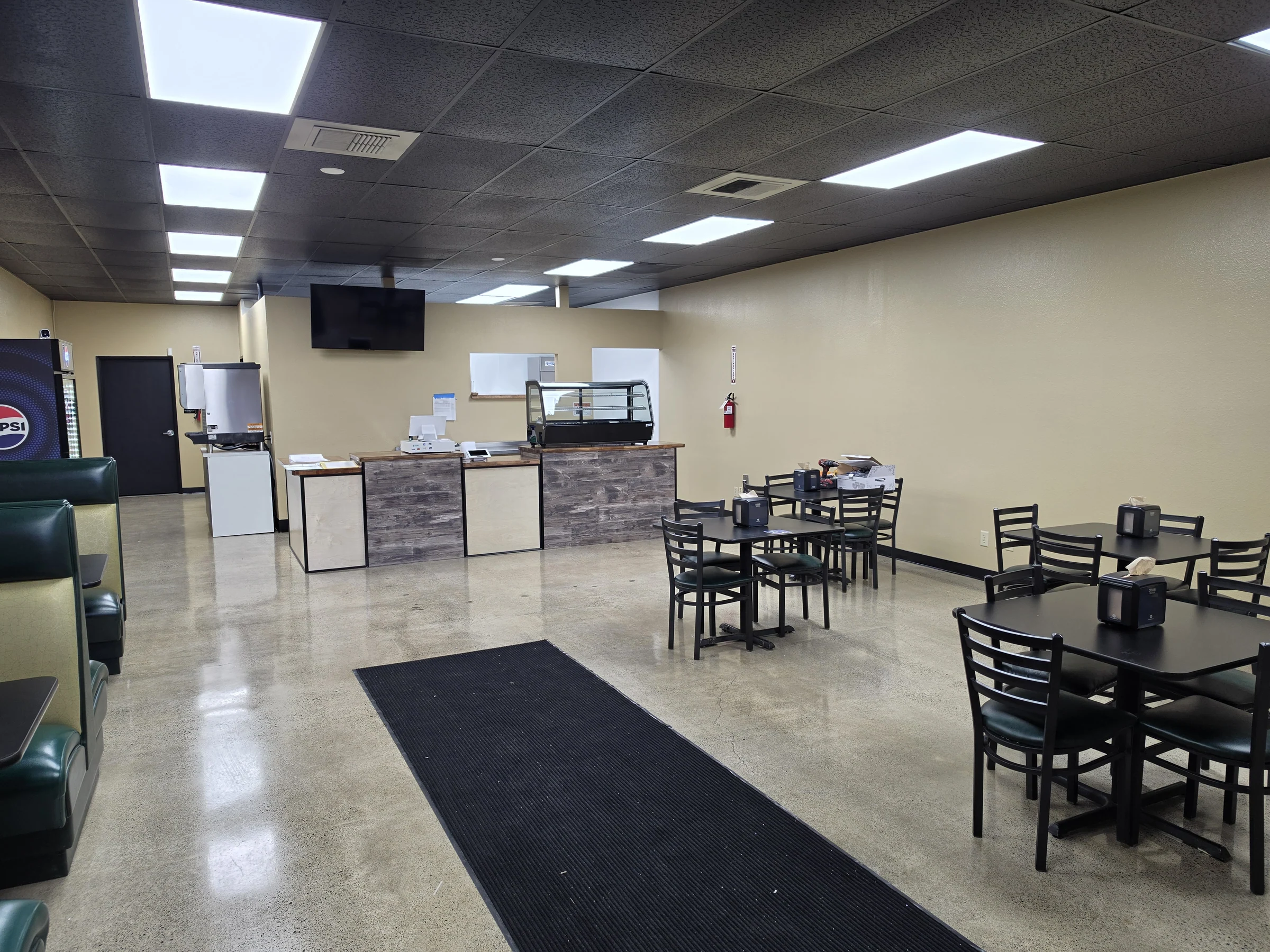 Finished restaurant dining space with tables, booths, service counter, and polished concrete floor at Benji’s Deli.