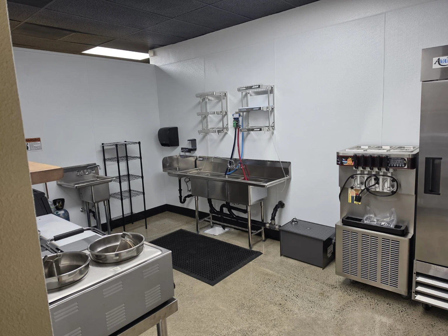 Commercial kitchen wash area at Benji’s Deli with stainless-steel sinks, shelving, and food-service equipment.