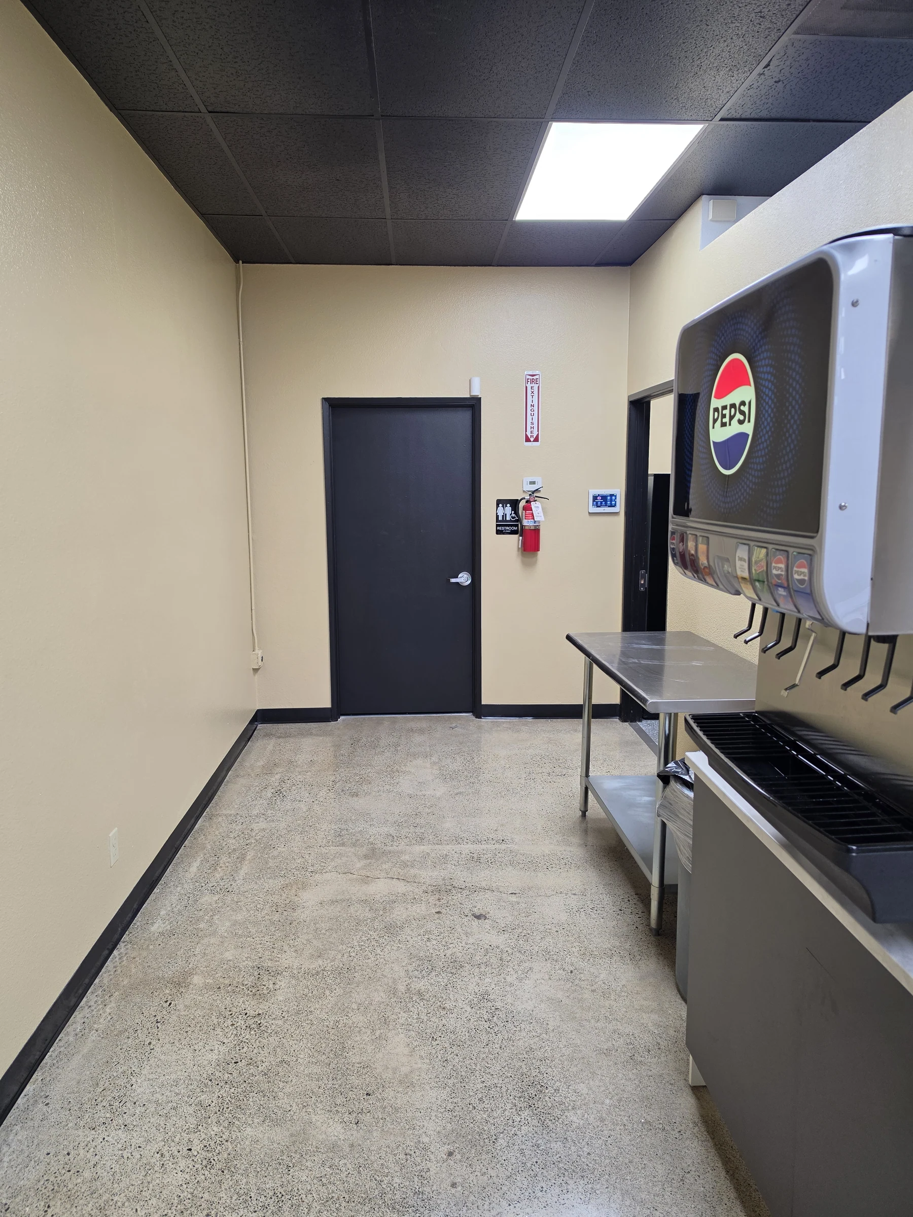 Beverage station at Benji’s Deli with soda fountain, stainless-steel table, black ceiling, and finished floor.