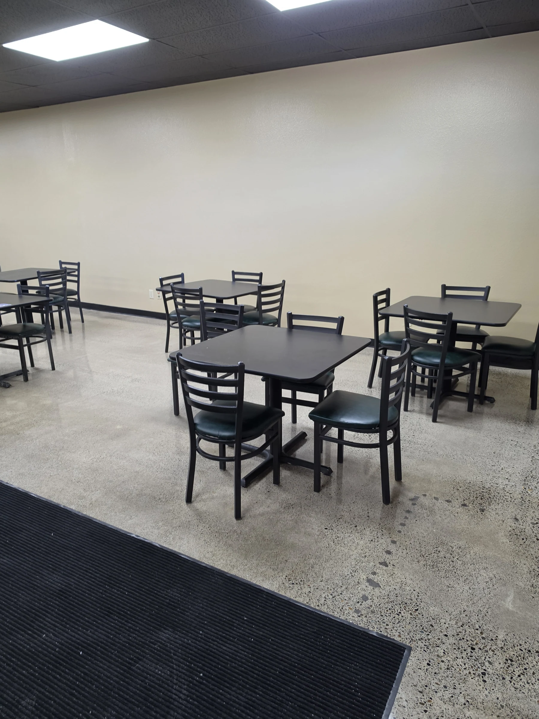 Guest seating at Benji’s Deli with black restaurant tables and chairs against finished light-colored walls.