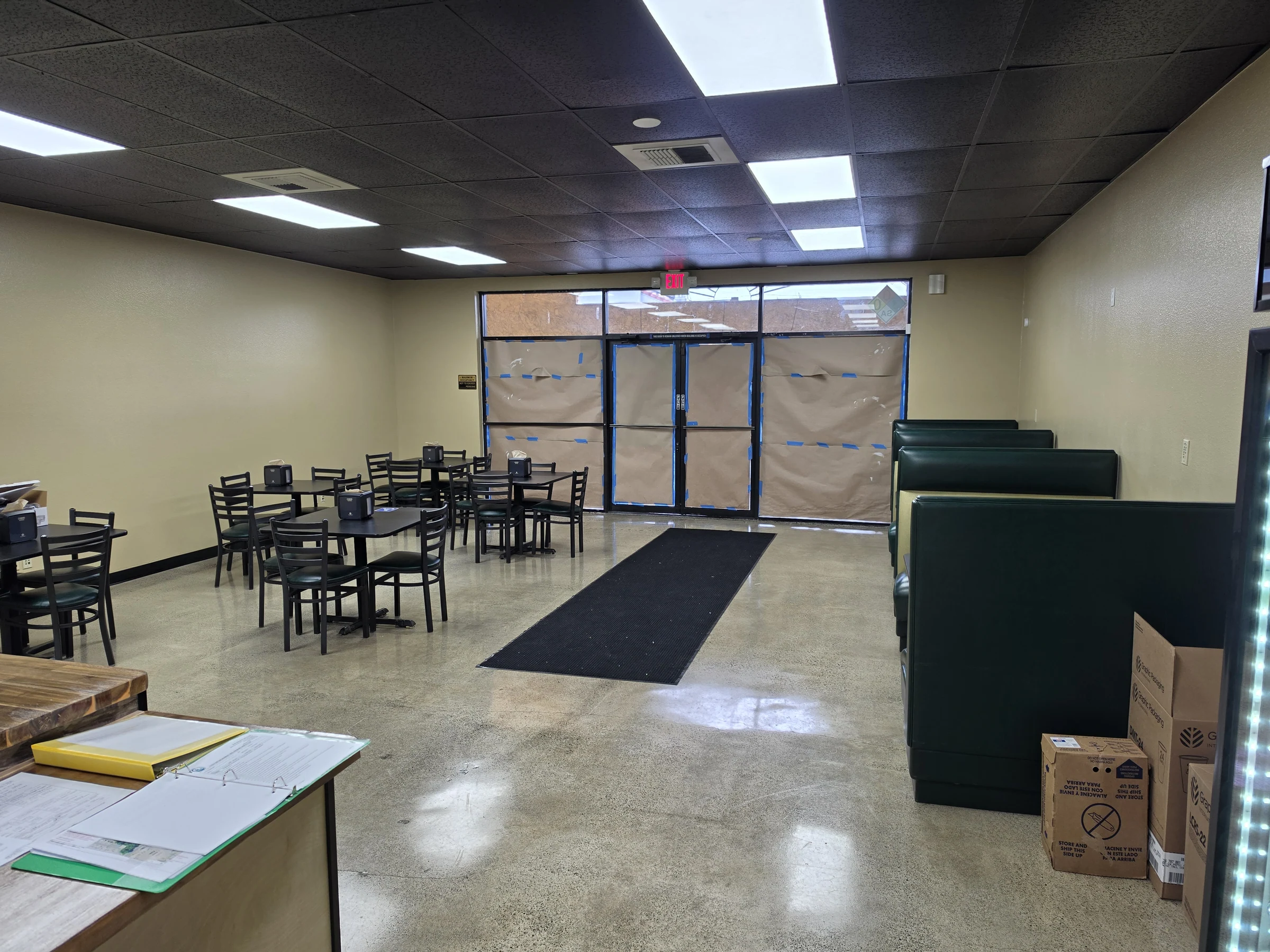 View from Benji’s Deli dining room toward front entry, showing booths, tables, lighting, and refinished floor.
